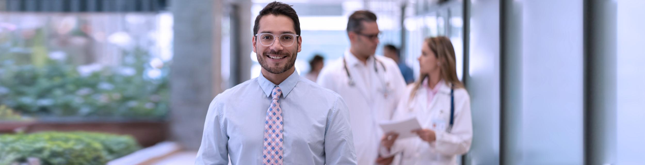 Gerente de hospital sonrie, en segundo plano se encuentran doctores dialogando de un caso