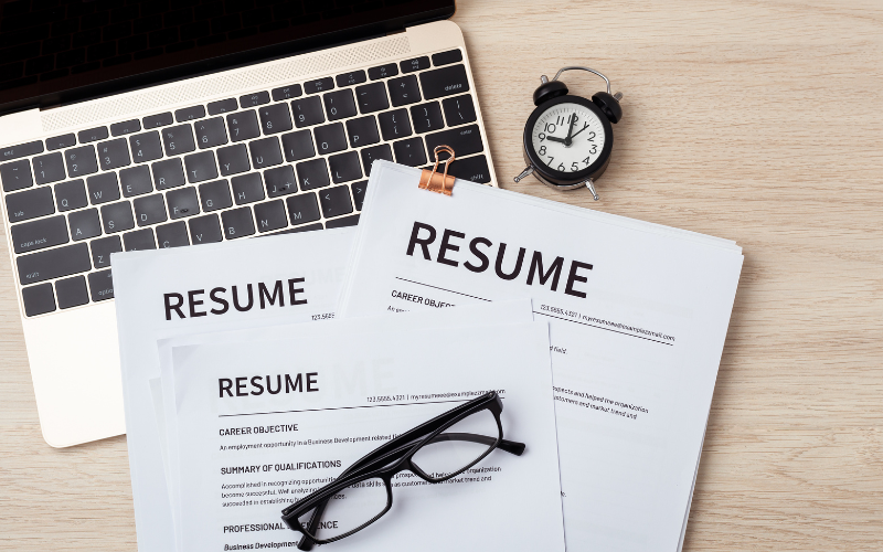 Computadora con resumes impresos y un reloj